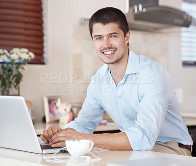 Buy stock photo Portrait of a handsome male sitting in his kitchen with a cup of coffee browsing on his laptop