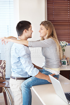 Buy stock photo A happy couple embracing in their kitchen with a laptop on the kitchen counter
