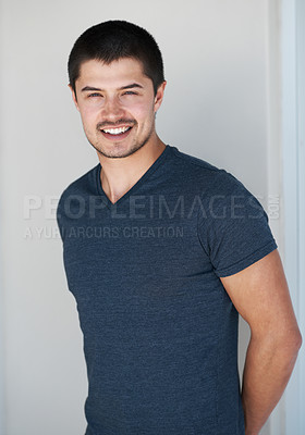 Buy stock photo Happy, portrait and man smile with student clothes, style and modern house with white wall and casual fashion. Confidence, calm and cool clothing in a home with trendy and relaxed male tshirt