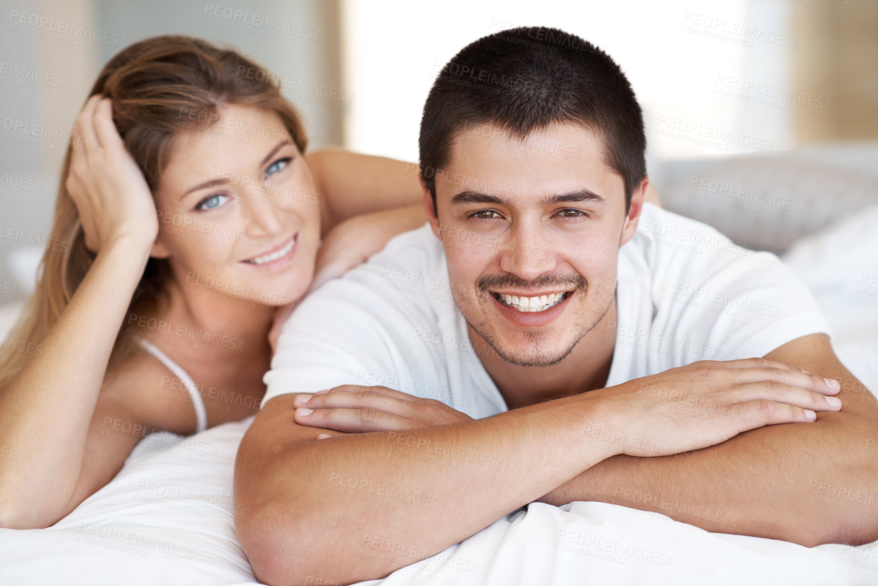 Buy stock photo Attractive young couple lying in bed together with broad smiles