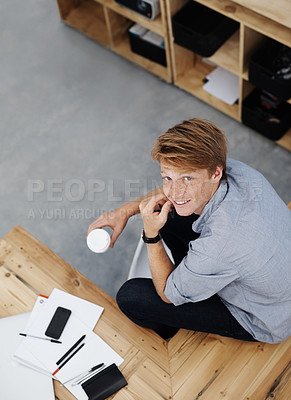 Buy stock photo Portrait of a young businessman from above, holding a coffee cup and sitting in the office. A handsome male student taking a study break after lectures. One designer relaxing in a creative workplace