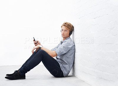 Buy stock photo Floor, portrait and man with smartphone with headphone for music, radio podcast and streaming online for playlist. Indoor, male person and phone for mobile app, song and audio track to relax by wall