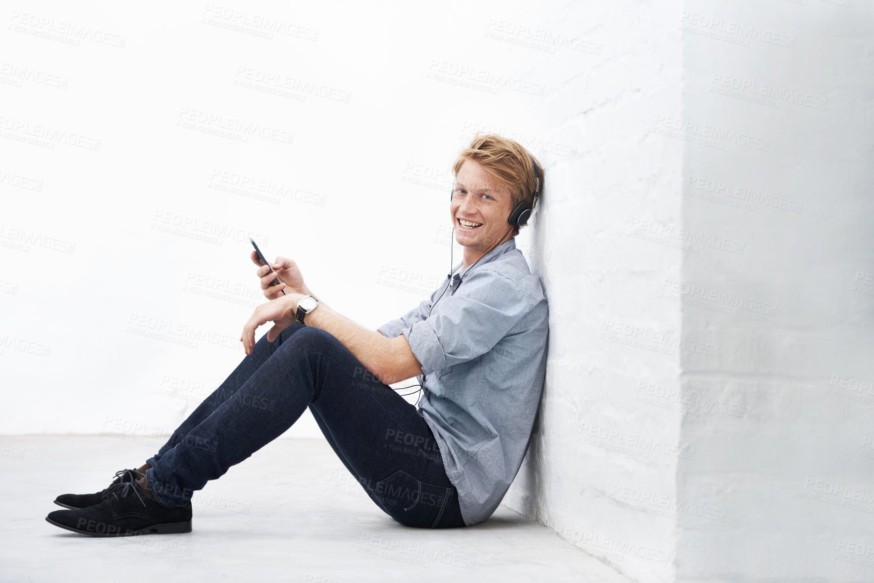 Buy stock photo Floor, portrait and happy man with smartphone for music, radio podcast and streaming online for playlist. Indoor, male person and headphone for mobile app, song and audio track to relax by wall