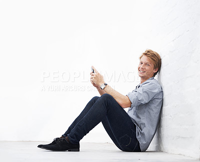 Buy stock photo Man, phone and floor with space by wall in portrait, communication or texting app with smile. Young businessman, entrepreneur and happiness sitting with smartphone in mock up for social media chat