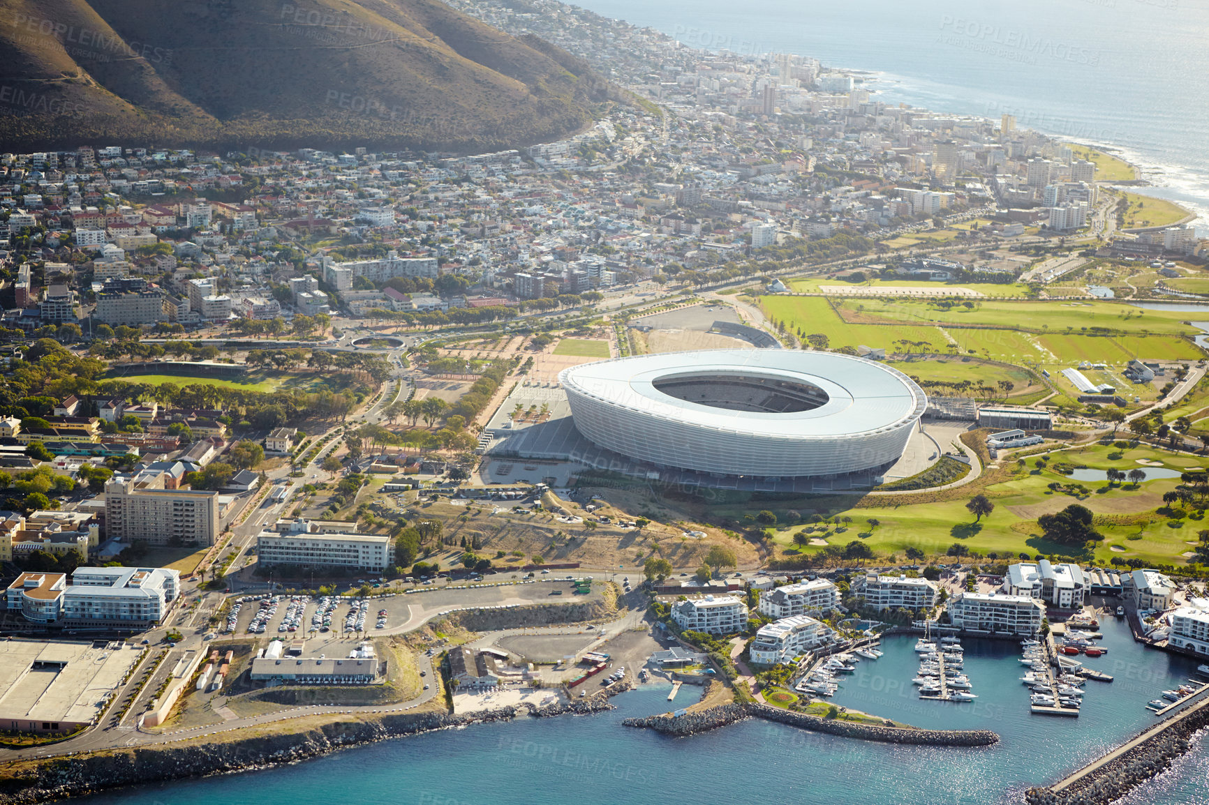 Buy stock photo Harbor, drone and stadium in city for travel with ships, cruise or buildings by ocean and mountain. Boats, coast and aerial view of infrastructure by seashore for holiday destination in Cape Town.