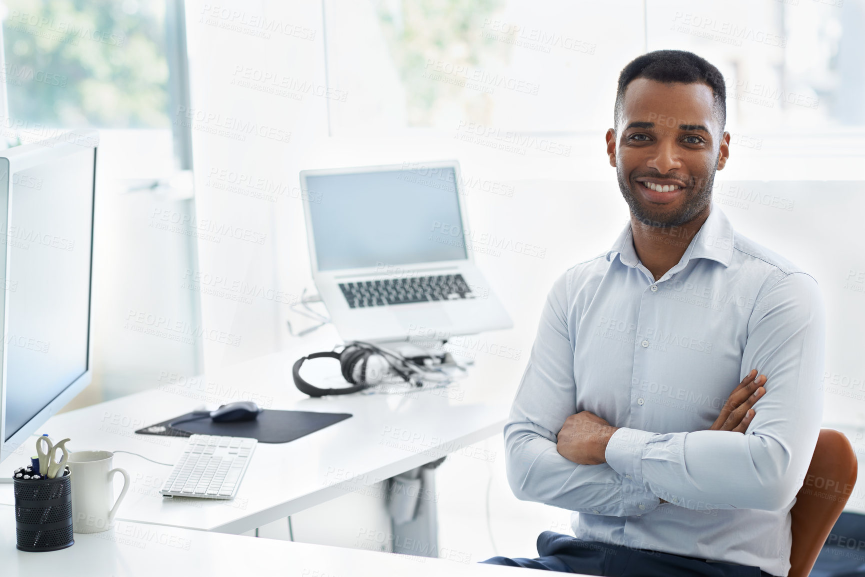 Buy stock photo A handsome young african american businessman sitting at his desk with his arms folded