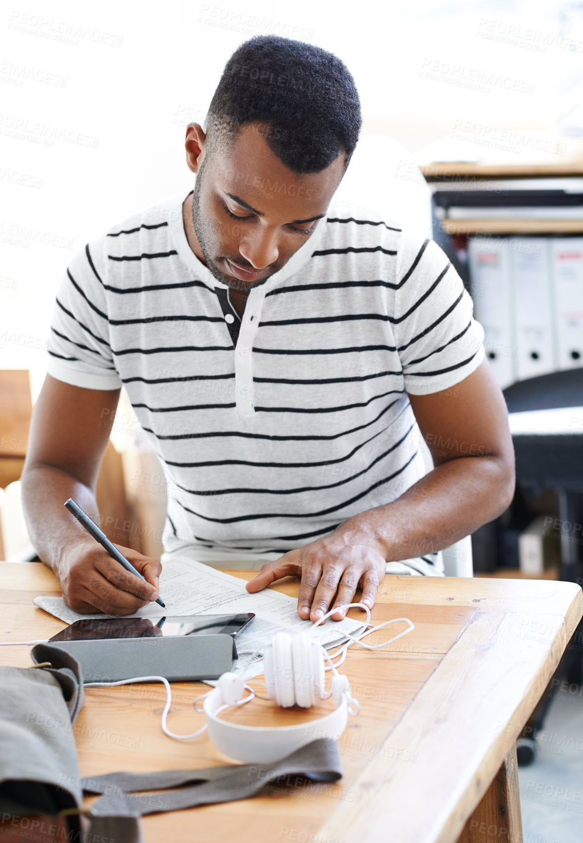 Buy stock photo Black man, newspaper and job search in startup office, tablet and research for notes of information. Male person, entrepreneur and documents for feedback report, writing ideas and strategy or letter