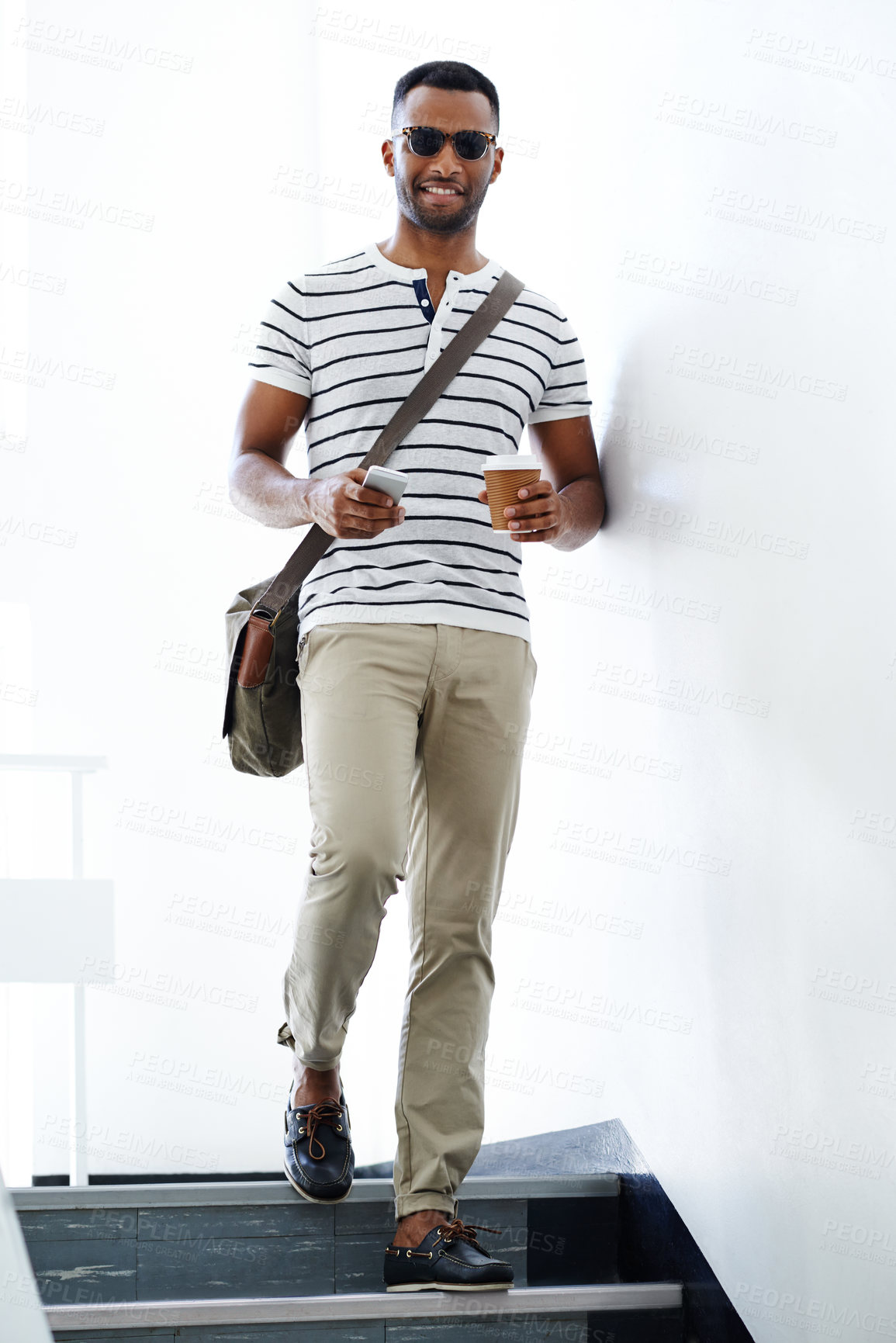 Buy stock photo A stylish, casually attired young businessman walking down the stairs while holding his mobile and coffee