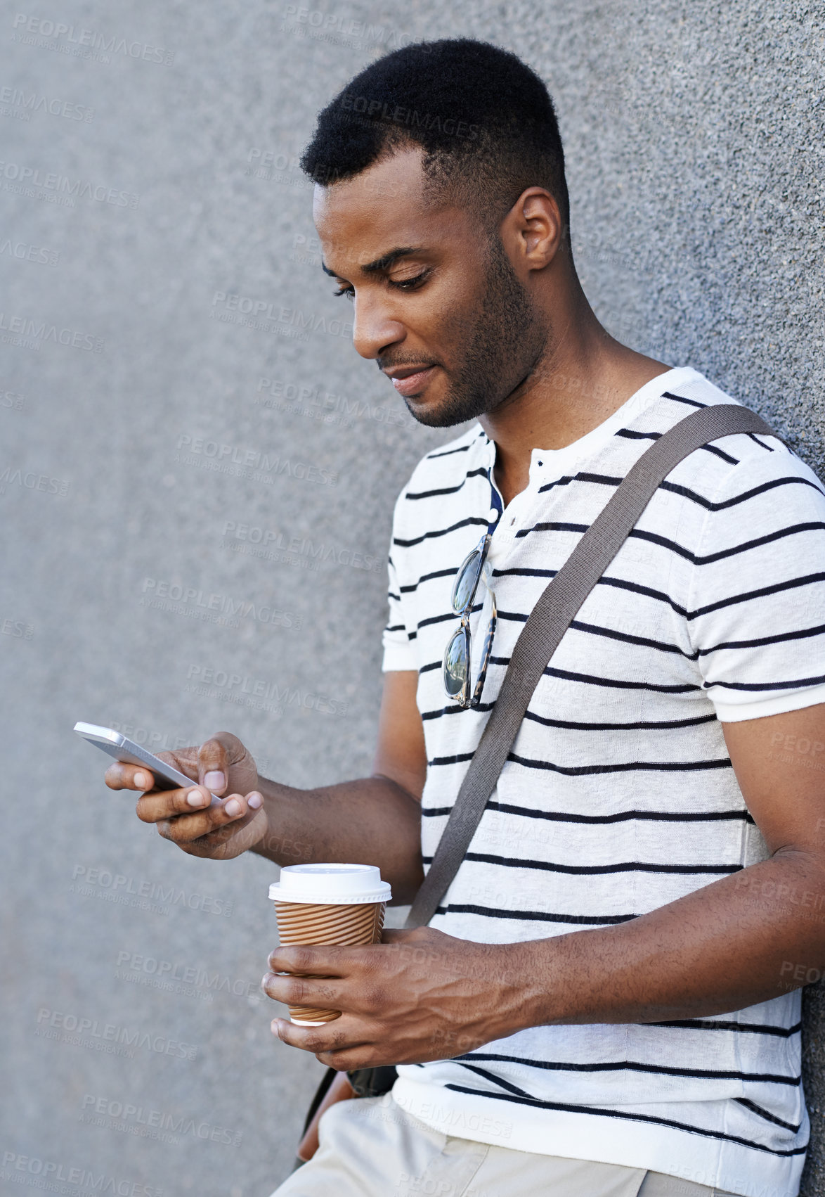 Buy stock photo A handsome african american businessman leaning against a wall in the city while using his mobile