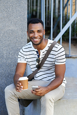 Buy stock photo A handsome casually dressed african american businessman sitting in the city and using his mobile while drinking coffee