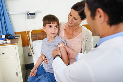 Buy stock photo A young boy admiring his doctor as he puts a plaster on his arm