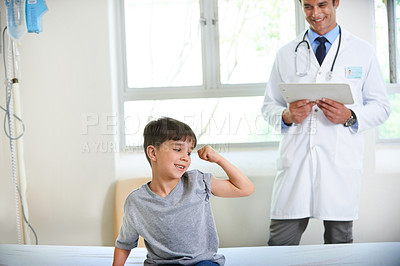 Buy stock photo Shot of a young boy playfully flexing his arm under his doctor's watchful eye
