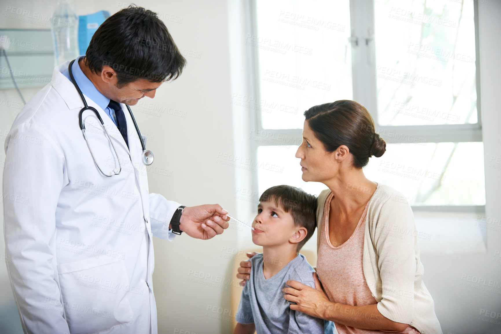 Buy stock photo The family doctor takes a young boy's tempreture while his mother holds him