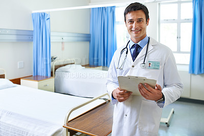 Buy stock photo Portrait of a handsome young doctor standing with a clipboard in a hospital ward