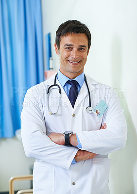 Buy stock photo Portrait of a handsome young doctor standing with his arms folded in a hospital ward