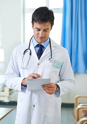 Buy stock photo Shot of a handsome young doctor using a tablet