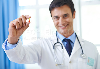 Buy stock photo Shot of a handsome young doctor holding up a capsule tablet