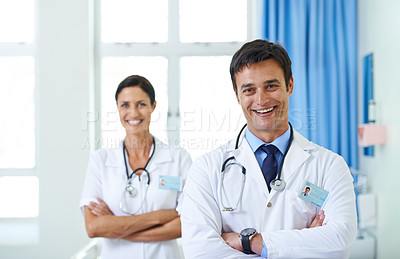 Buy stock photo Portrait of a handsome young doctor with his nursing assistant in the background