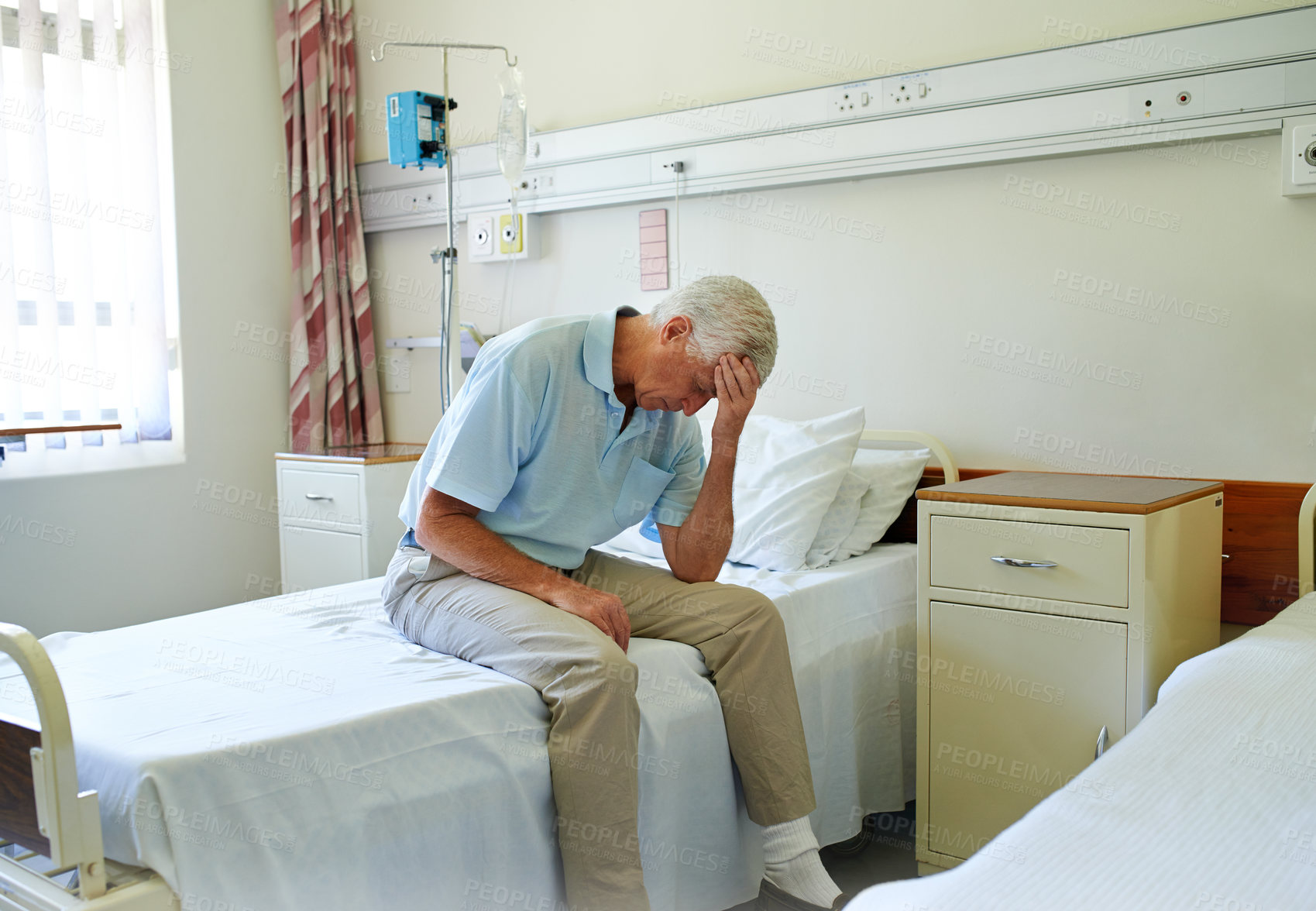 Buy stock photo Shot of a senior man in pain sitting alone on a bed in a hospital ward