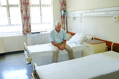 Buy stock photo Shot of a senior man sitting alone on a bed in a hospital ward