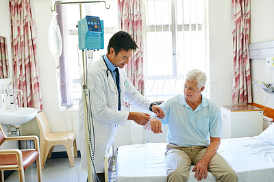 Buy stock photo Shot of a handsome young doctor attending to a senior man in a hospital ward
