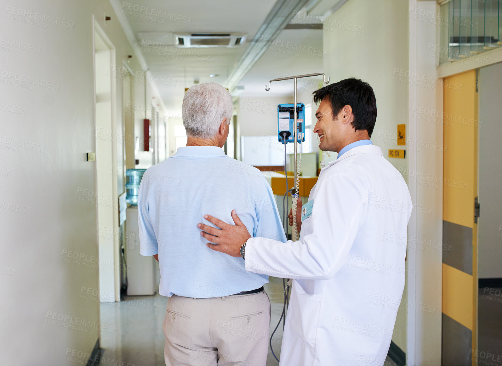 Buy stock photo Shot of a handsome young doctor walking with his senior patient down the hall