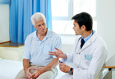 Buy stock photo Shot of a handsome young doctor explaining medication to a senior patient