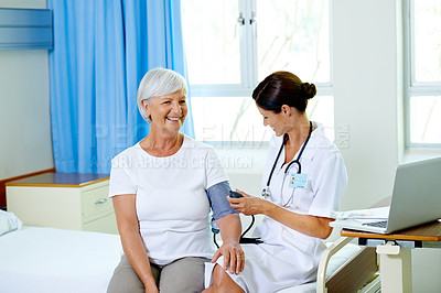Buy stock photo Shot of a beautiful young female doctor testing a senior patient's blood pressure