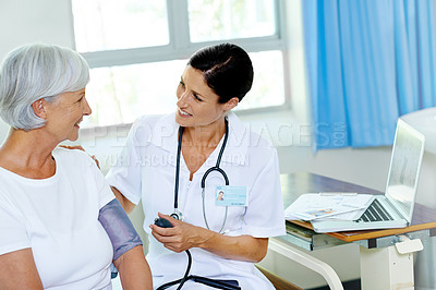 Buy stock photo Shot of a beautiful young female doctor testing a senior patient's blood pressure