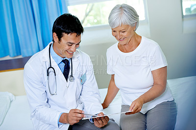 Buy stock photo Shot of a handsome young doctor going through a chart with a senior patient