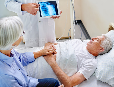 Buy stock photo Shot of a sick man in a hospital bed being shown an xray of his shoulder while his wife holds his hand