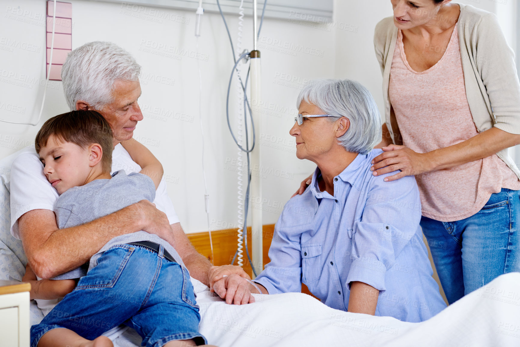 Buy stock photo Shot of a sick man in a hospital bed getting a hug from his grandson while family look on