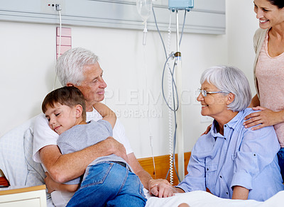 Buy stock photo Shot of a sick man in a hospital bed getting a hug from his grandson while family look on