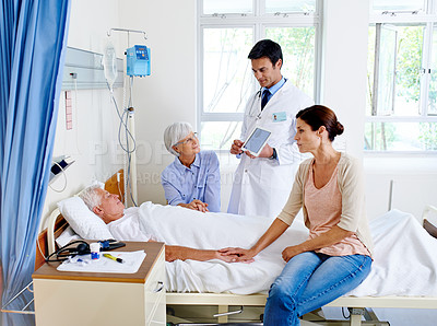 Buy stock photo Shot of a doctor delivering results to a sick man in a hospital bed and his family