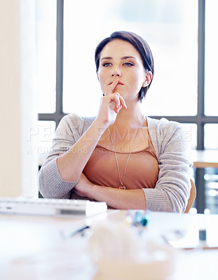 Buy stock photo Shot of an attractive young woman sitting and thinking at her desk in an office