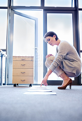 Buy stock photo Shot of an attractive young woman looking at papers lined up on the floor