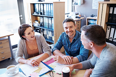 Buy stock photo High angle shot of three coworkers talking around a table