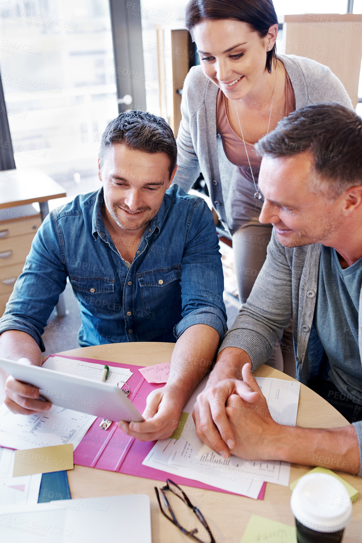 Buy stock photo Shot of three coworkers in a meeting looking at a tablet