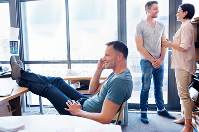 Buy stock photo Shot of a laid back member of an office team taking a break while two coworkers have a discussion in the background