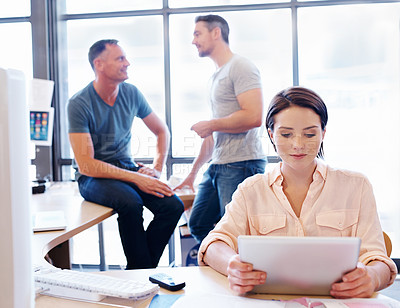 Buy stock photo Shot of an office worker using a tablet while her coworkers have a discussion in the background