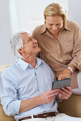 Buy stock photo Shot of a senior man looking at his wife while she points at his digital tablet