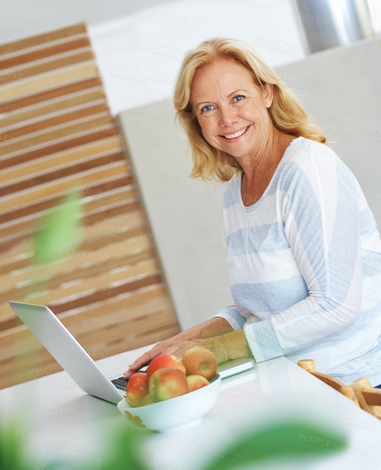 Buy stock photo Portrait of a senior woman sitting in her kitchen using a laptop