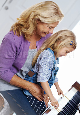 Buy stock photo Shot of a girl sitting on her grandmother's lap while playing piano