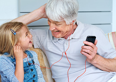 Buy stock photo Shot of an adorable little girl listening to music from a cellphone with her grandfather
