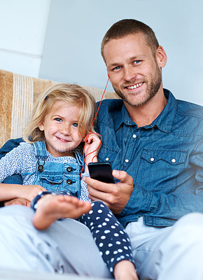 Buy stock photo Portrait of an adorable little girl sitting on the sofa sharing headphones with her father