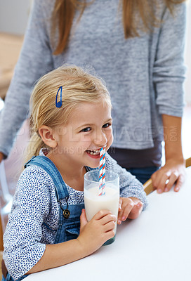 Buy stock photo Shot of a little girl enjoying a glass of milk while her mother stands nearby