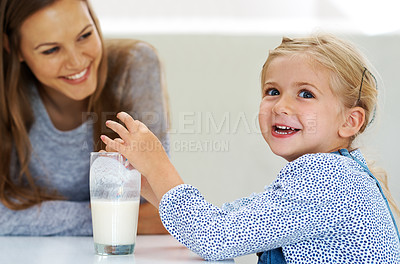 Buy stock photo Shot of a cute little girl enjoying a glass of milk with her mother sitting nearby