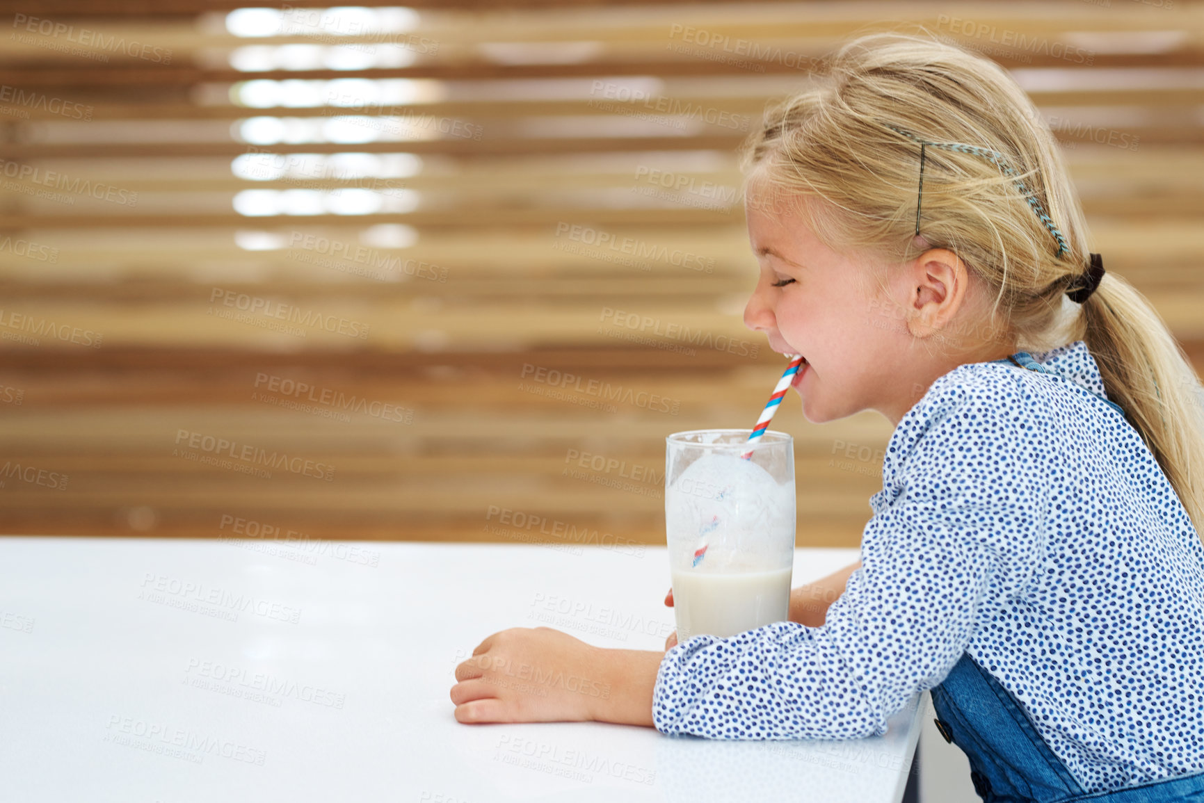 Buy stock photo Girl, child and drinking milk in home, laughing and vitamin d liquid for growth development. Female person, kid and glass of mineral juice for calcium at kitchen table, dairy breakfast and profile