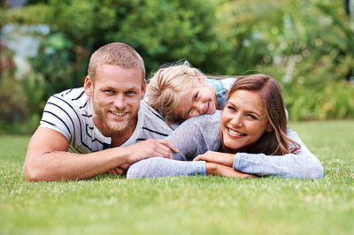 Buy stock photo Portrait of a happy family of three lying outside on the grass