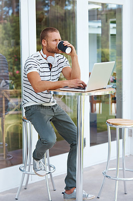 Buy stock photo Shot of a handsome young man working on a laptop outside and drinking some coffee